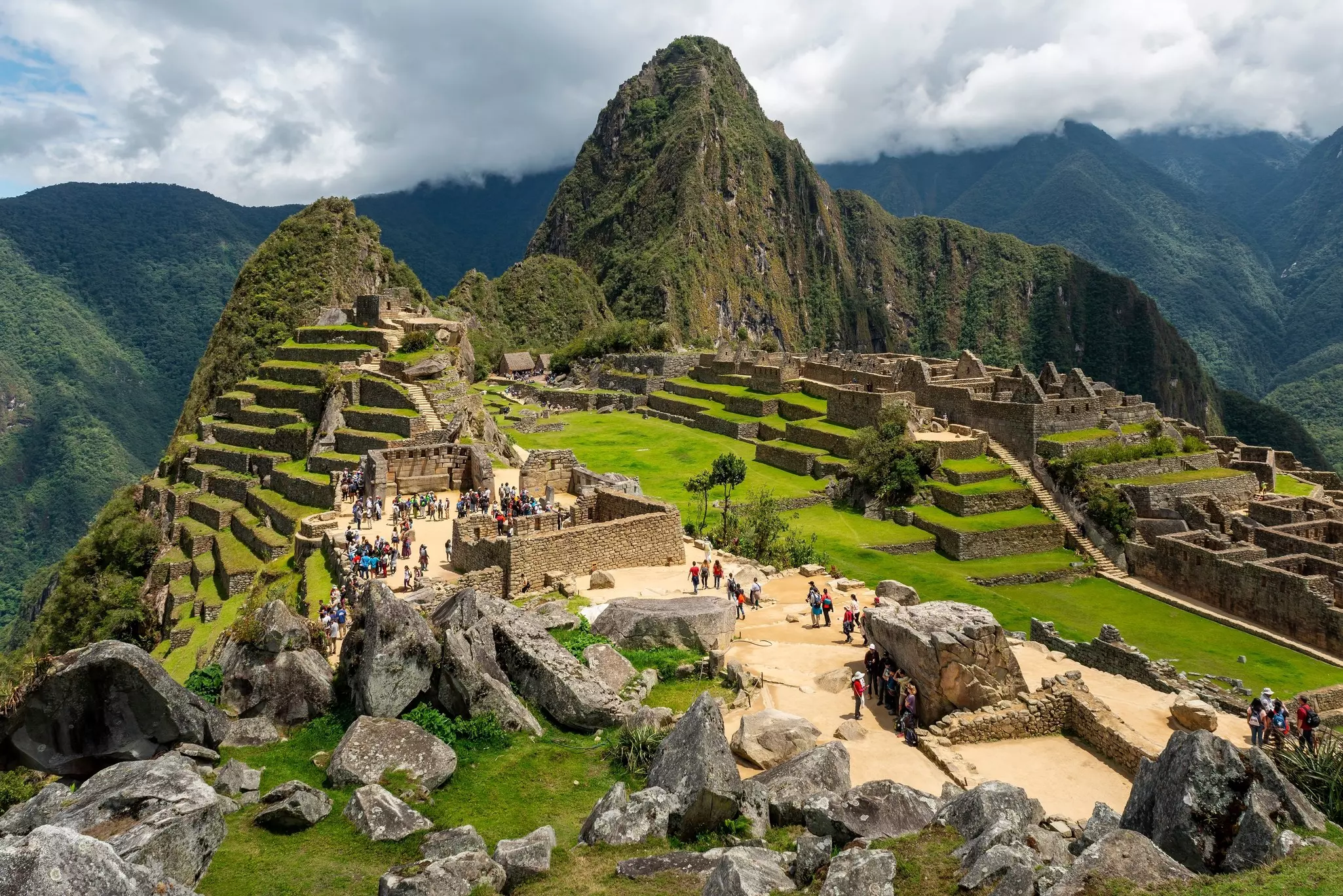 Machu Picchu ruins with tourists with dramatic clouds.