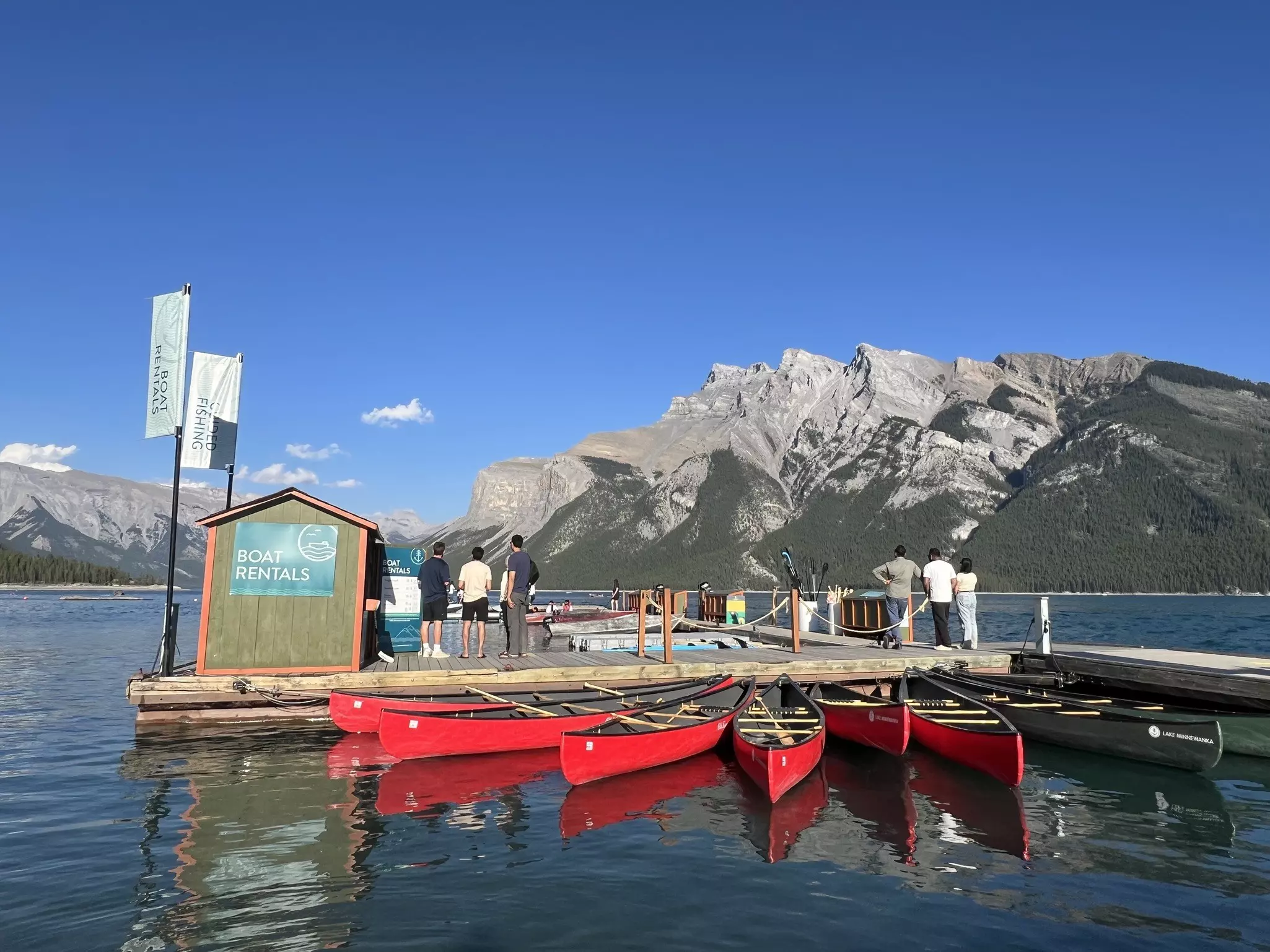 A boat rental shop at Lake Minnewanka with people on the dock and red boats nearby