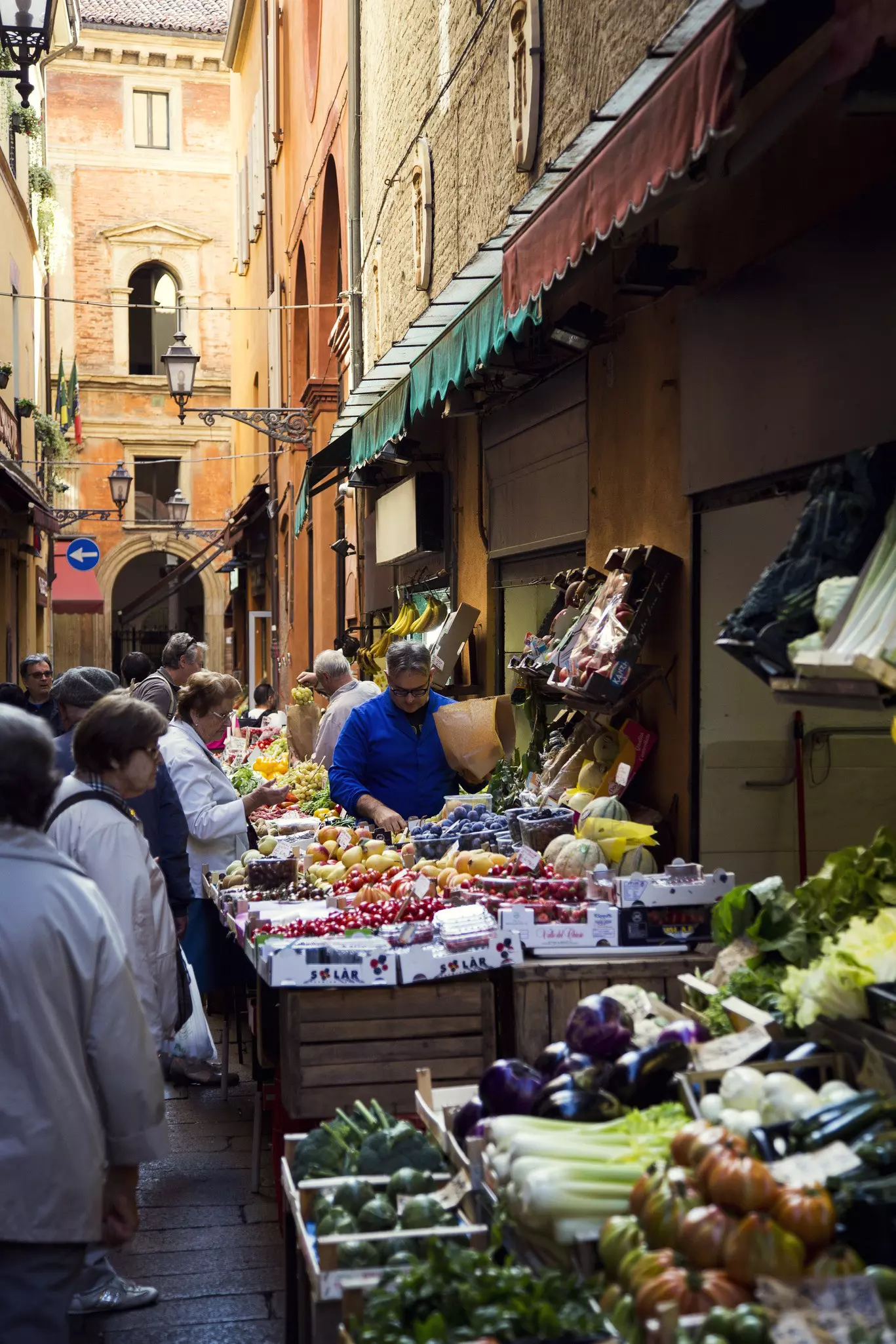 Passers-by look at fresh produce stalls at an outdoor market in Bologna.