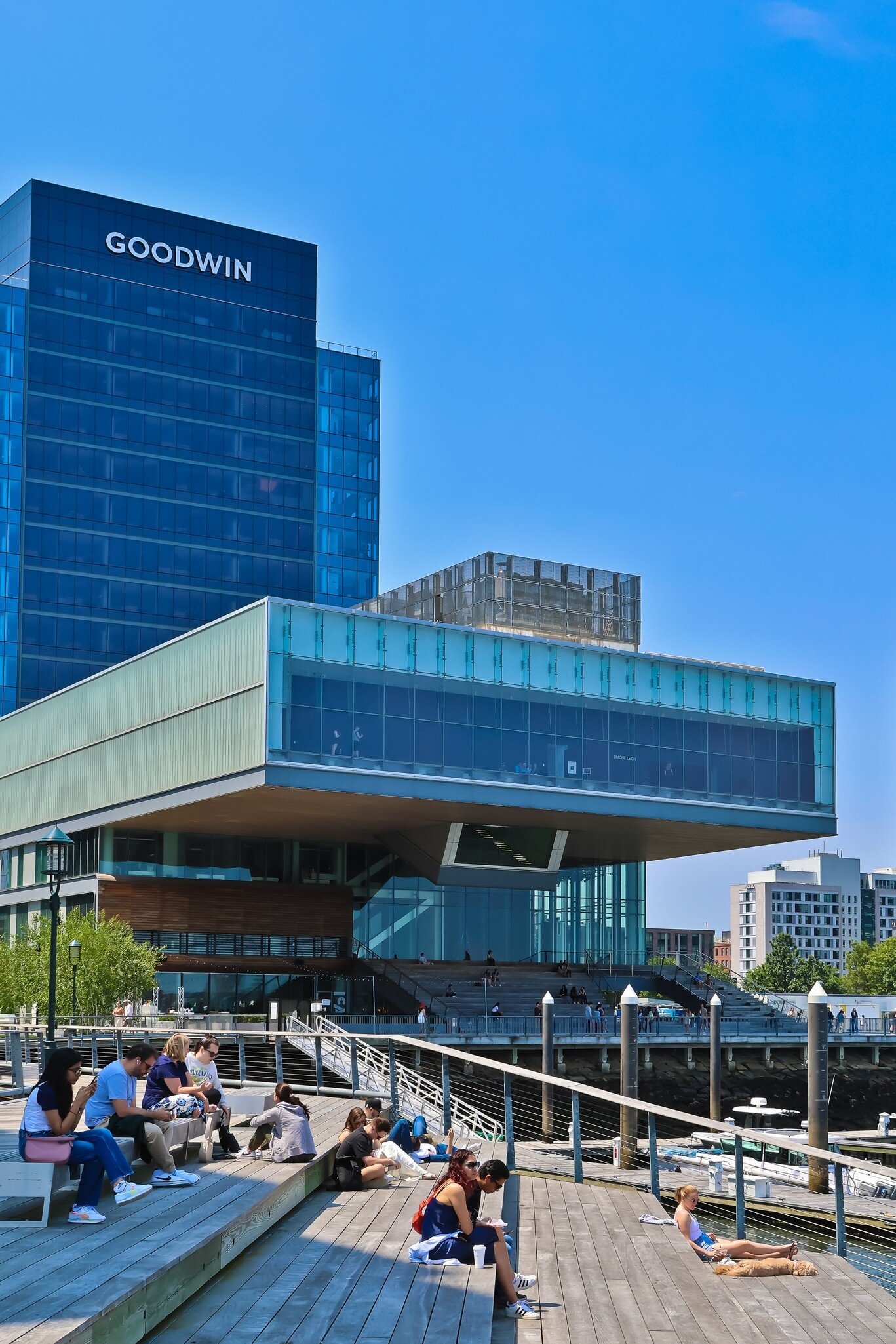 People resting by the water at Pier 4 in Boston Harbor, with the Institute of Contemporary Art in the background in Boston, Massachusetts.