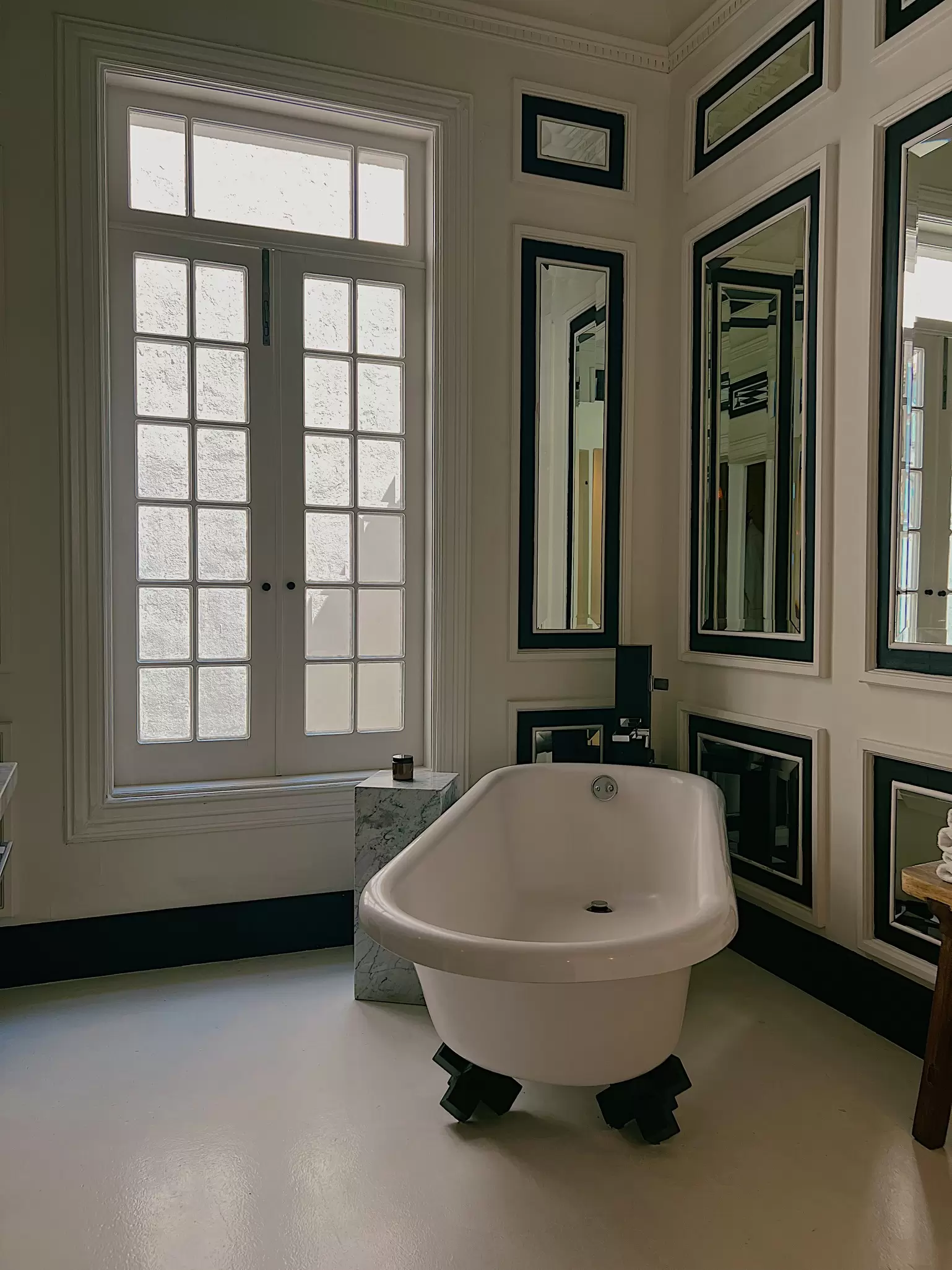 Bathroom with a claw foot tub with a large double window on one wall and mirrors on the other wall