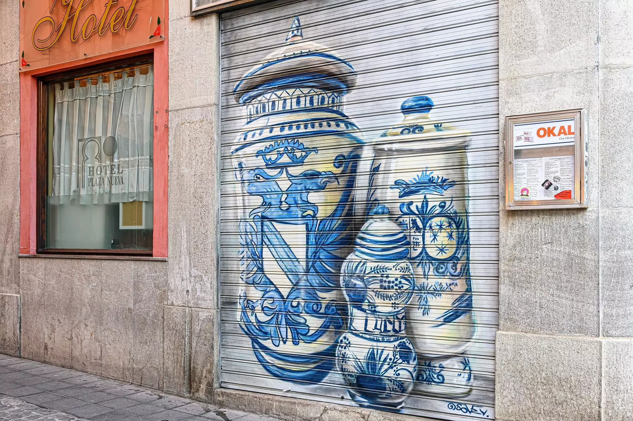 Urban art depicting blue-and-white containers painted on the closed doors of a pharmacy building.