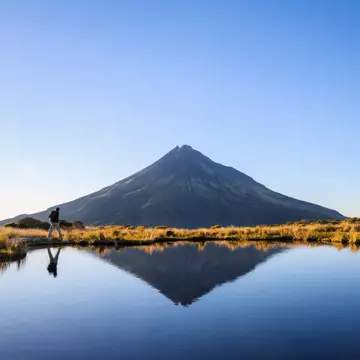 Man hiking the Pouakai circuit. Mt Taranaki under the clear blue sky. New Zealand.