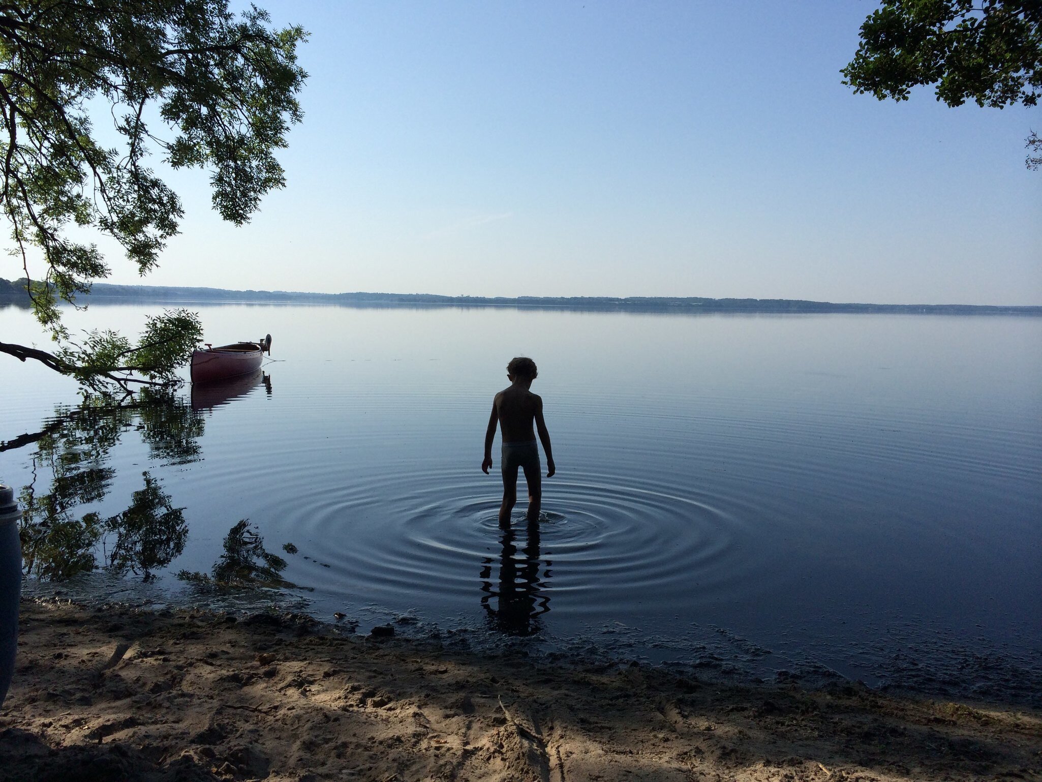 Silhouette of boy wading into the calm lake of Esrum in the early morning, Gribskov Region.