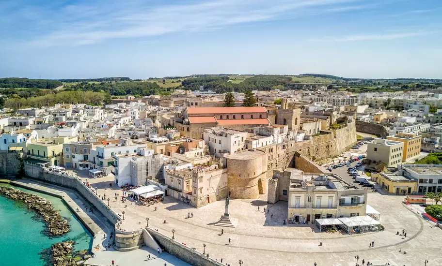 Aerial view of Otranto, Italy: the round-towered Aragonese castle, seafront piazza with statue and whitewashed old town