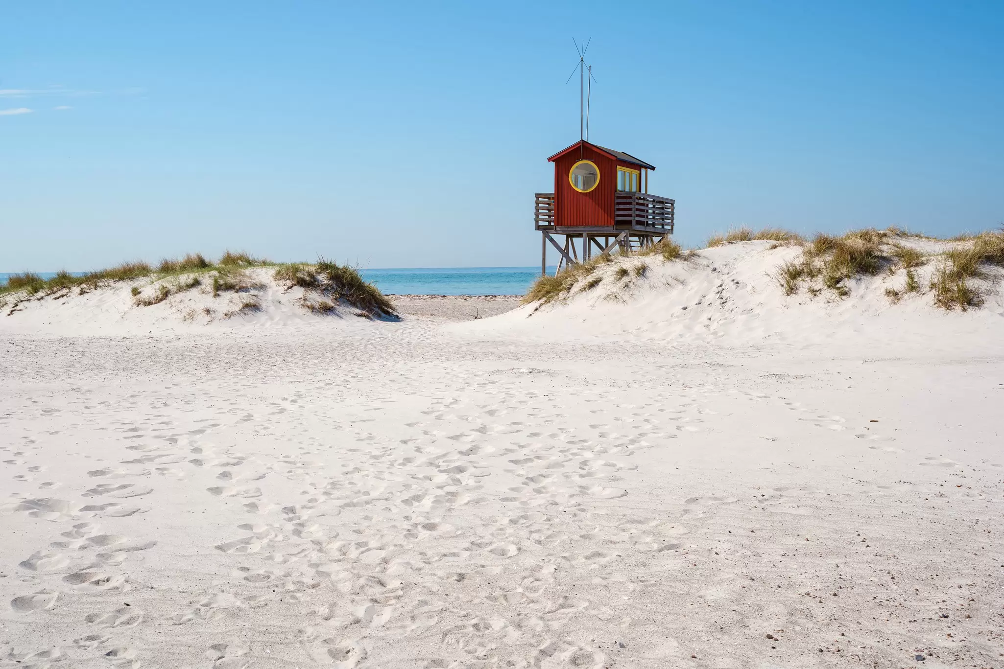 A red lifeguard tower at a sandy beach during the summer.
