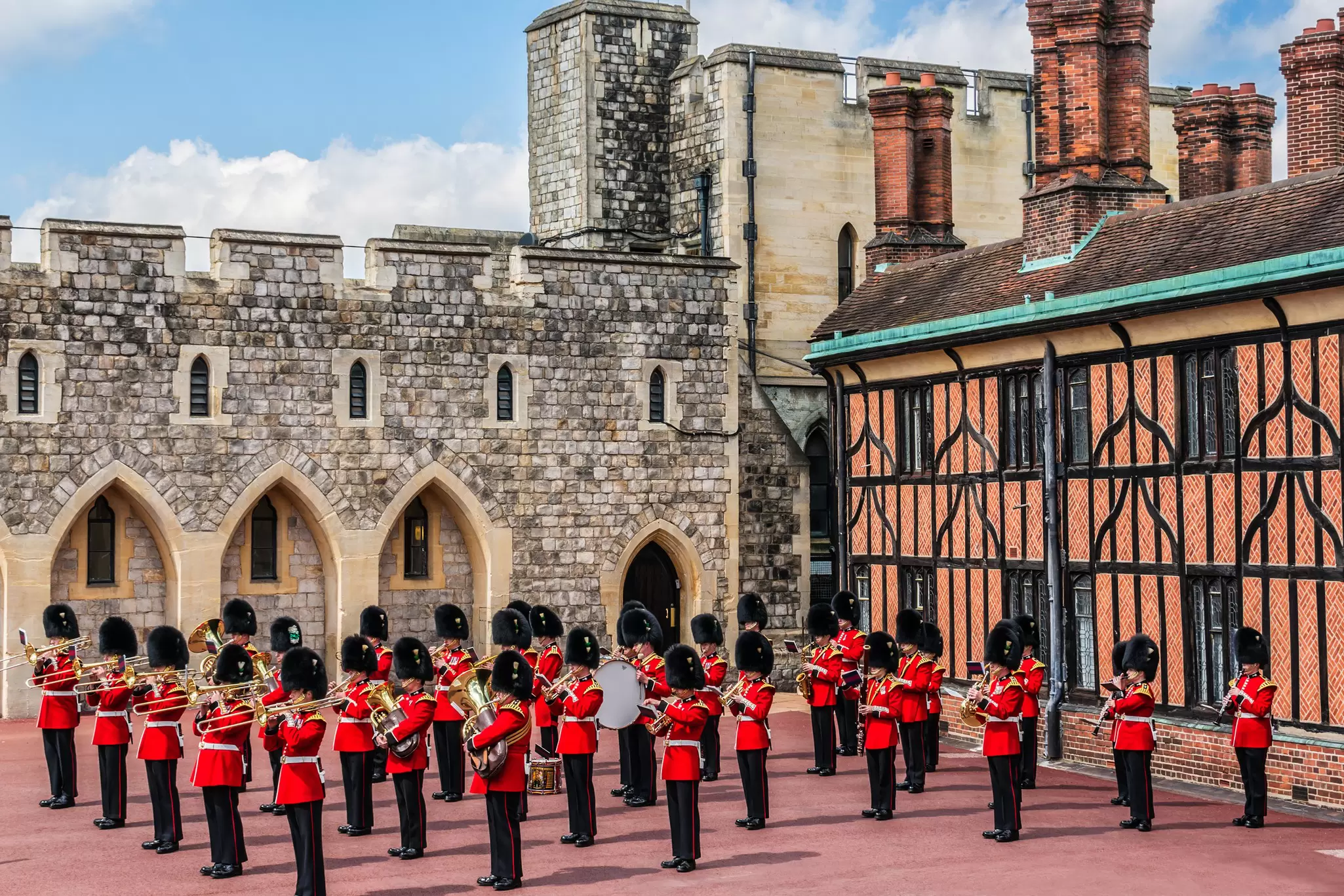 Rows of guards in red-and-black uniforms play musical instruments in a castle courtyard