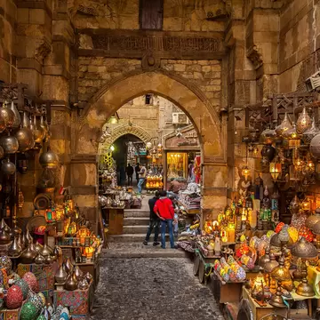 Lamps line the walls on either side of the path through the narrow market alleyway