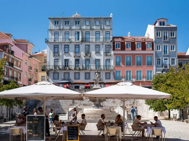 People gather under parasols in a sunny public square.