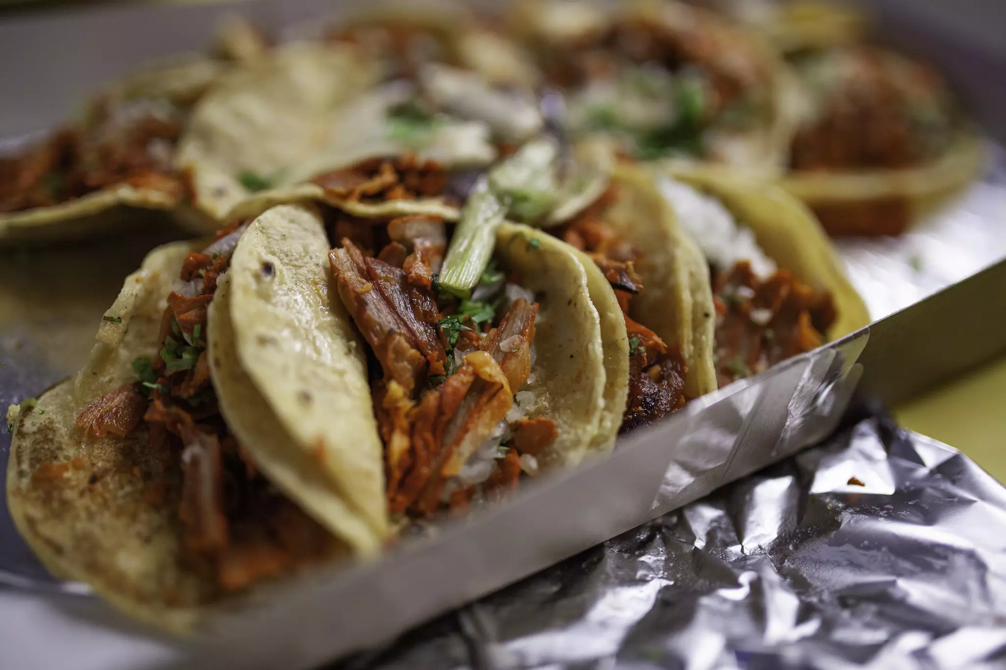 A plate of three al pastor tacos, with red meet and herbs on top.