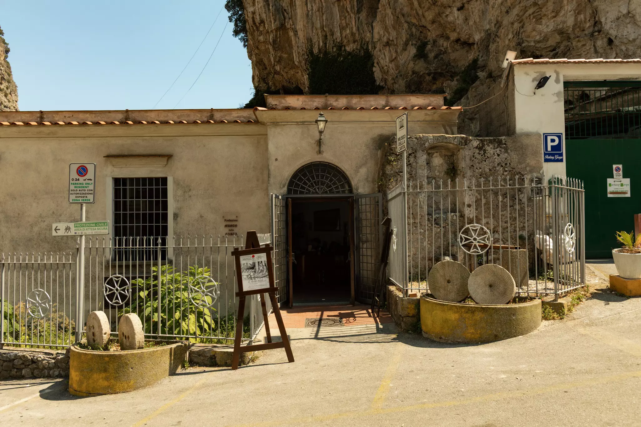 Exterior of a museum, a low-slung stone building nestled against a rocky cliff on a sunny day.