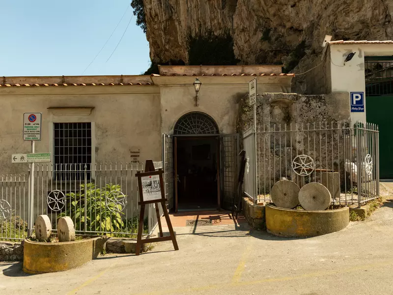 Exterior of a museum, a low-slung stone building nestled against a rocky cliff on a sunny day.