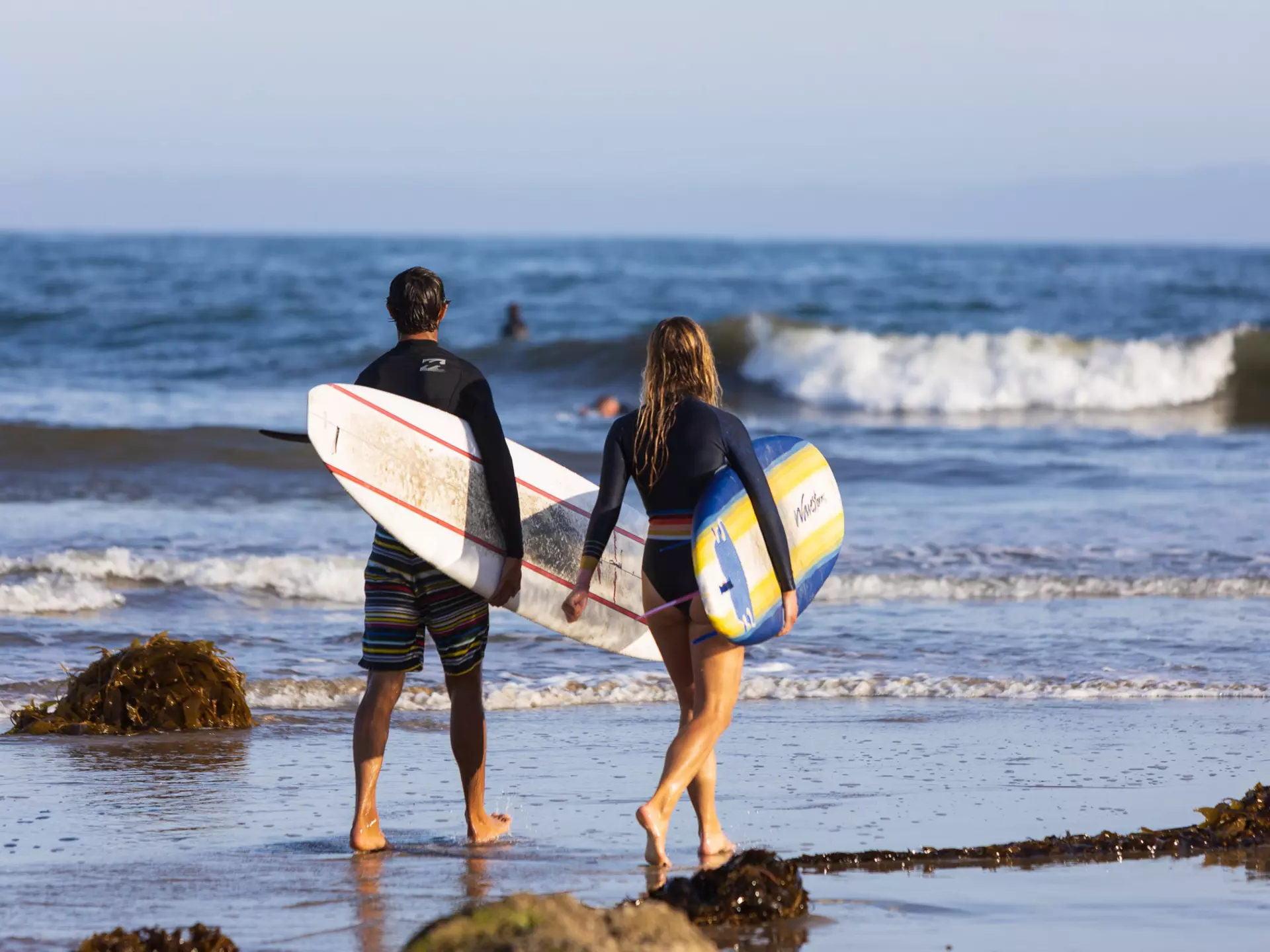 SANTA BARBARA, CA, USA - MAY 7,2020: Man and woman carrying surfboard on the beach going to the ocean. , License Type: media, Download Time: 2025-12-05T21:19:29.000Z, User: rhylton_redventures, Editorial: true, purchase_order: 65050 - Digital Destinations and Articles, job: Lonely Planet, client: social, other: Rhianydd Hylton