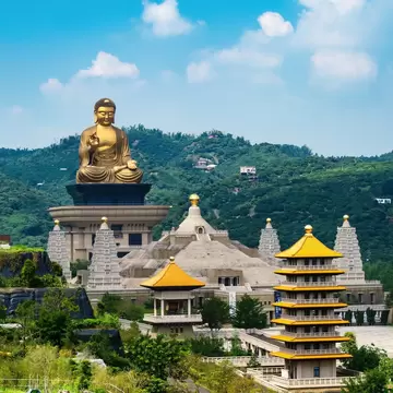 Golden buddha at the end of a row of yellow and gray pavilion buildings surrounded by green hillsides in Kaohsiung, Taiwan.