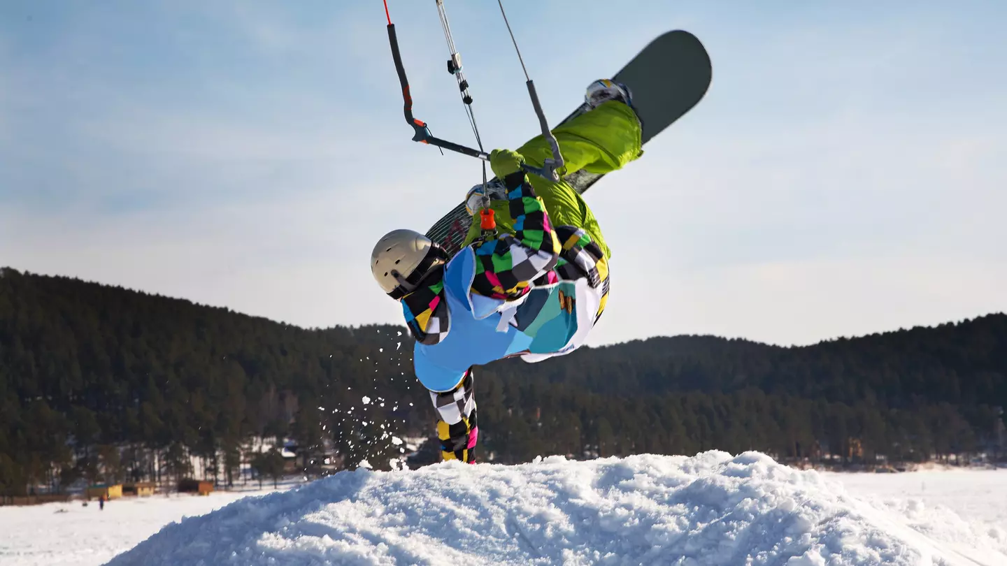 Man doing a handstand on a snowdrift while snowkiting on a frozen lake.