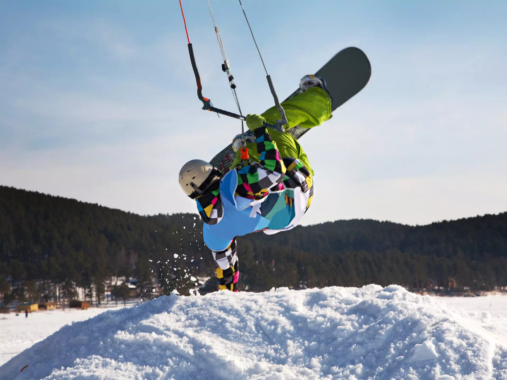 Man doing a handstand on a snowdrift while snowkiting on a frozen lake.