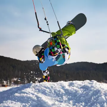 Man doing a handstand on a snowdrift while snowkiting on a frozen lake.