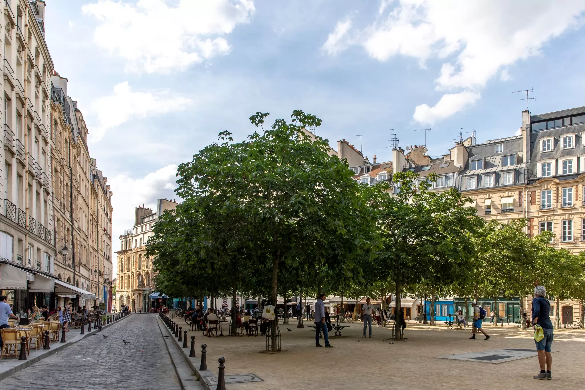 People playing petanque in a square of a city. In the background people eat on the terrace of the restaurants 