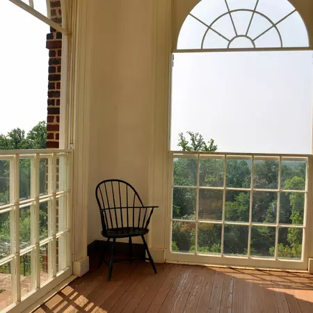 A chair inthe corner of a room with large open windows.