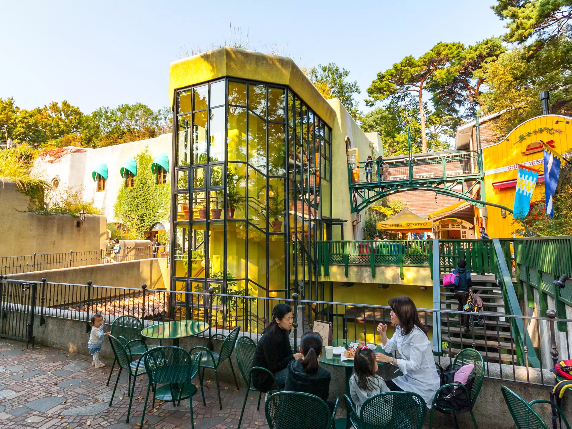 A family sits at a table in an outdoors museum complex with a toddler standing nearby