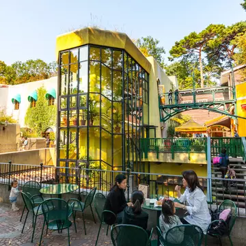 A family sits at a table in an outdoors museum complex with a toddler standing nearby