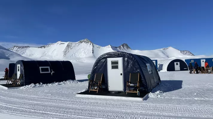 Large curved tents with doors and a small deck in a snow in front of mountains.
