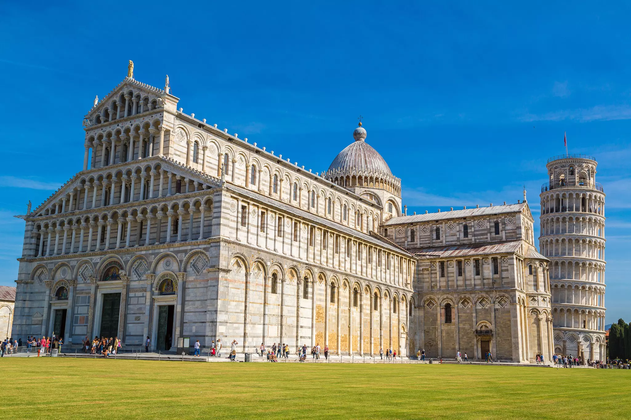 A huge marble church with a cental dome fills a city square. Behind is a towere with a distinctive lean.