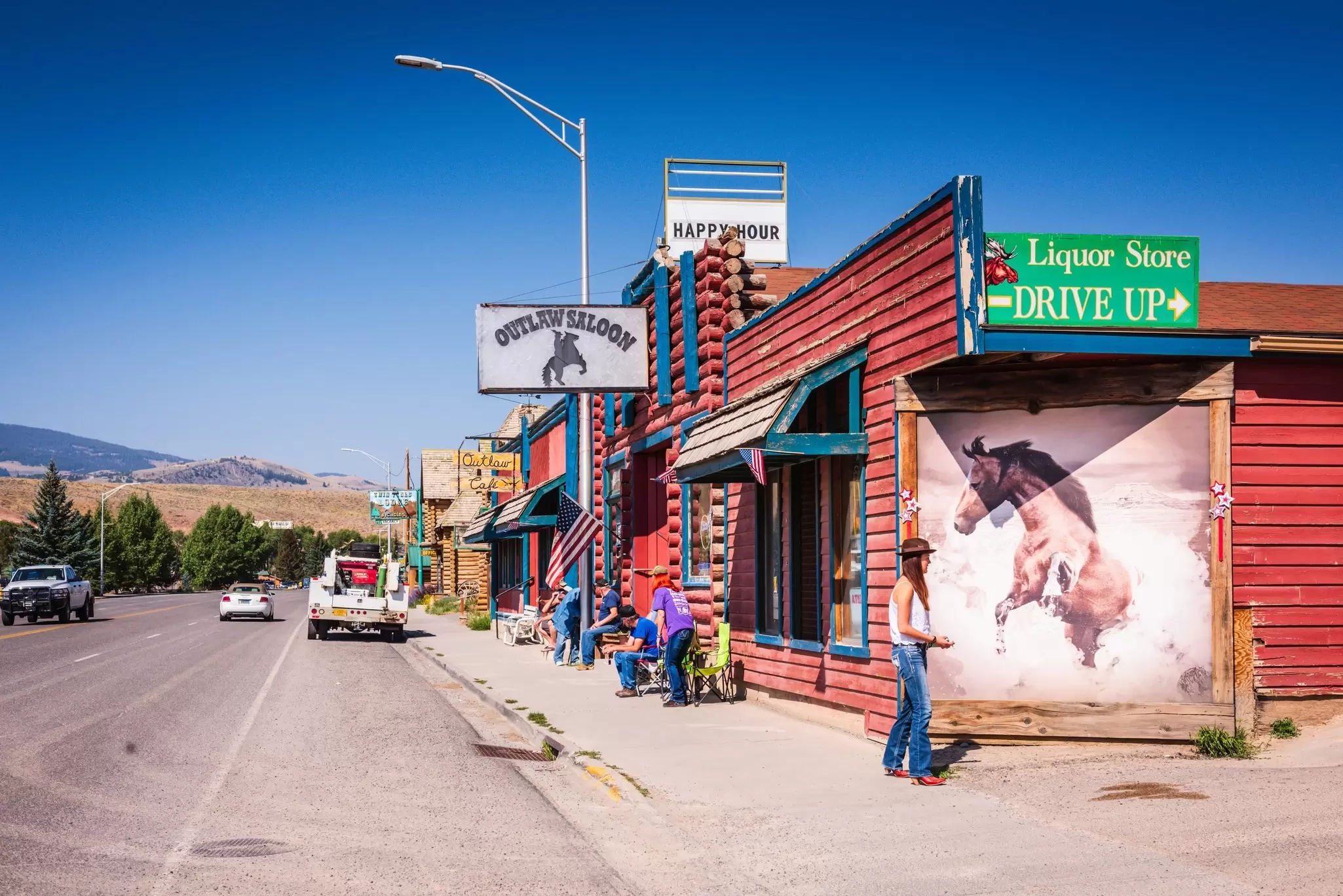 A street scene in Dubois, Wyoming, with people outside a bar and rocky hills in the background. 