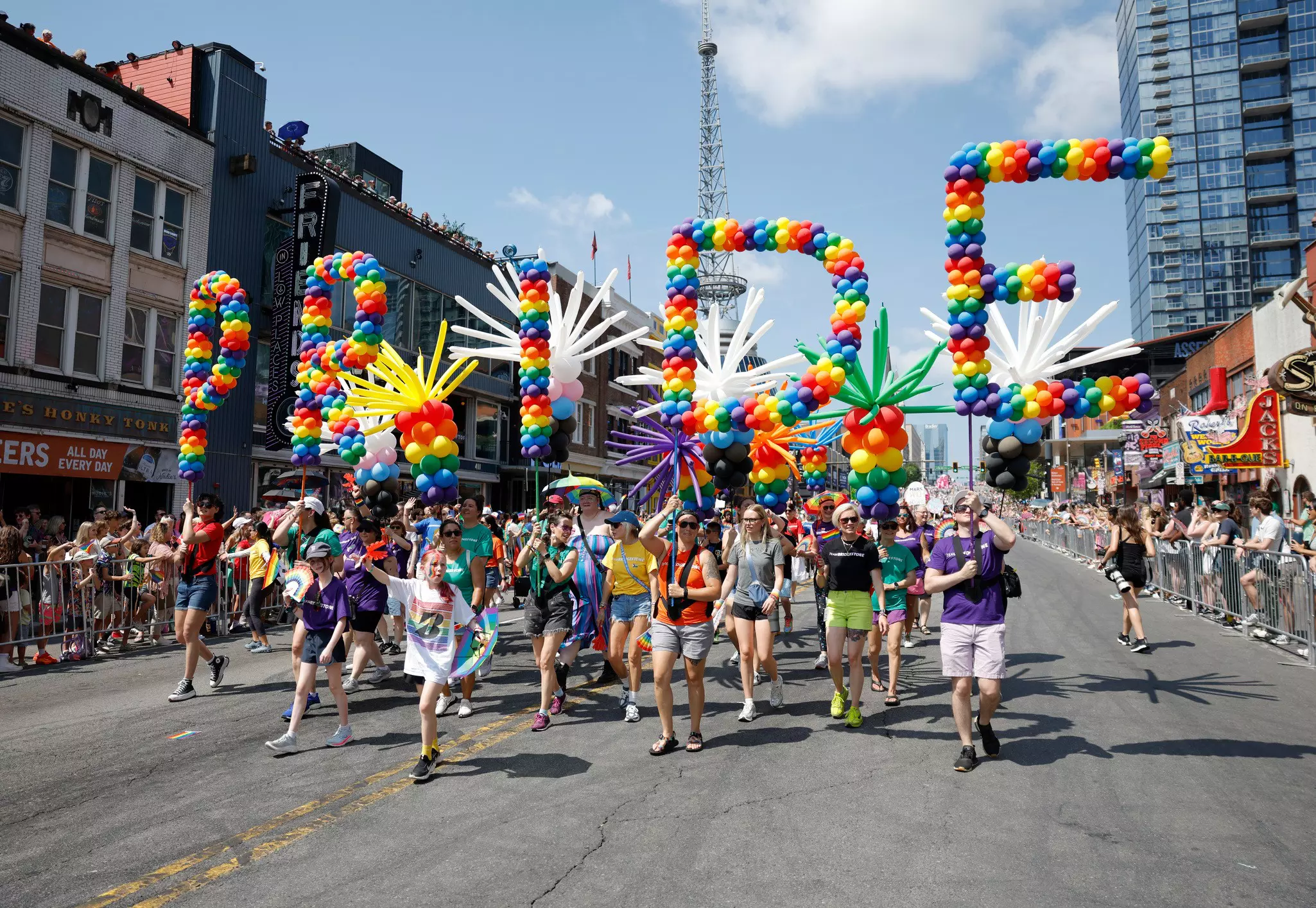 People march in a parade on a city street holding balloons that spell out the letters “P-R-I-D-E”