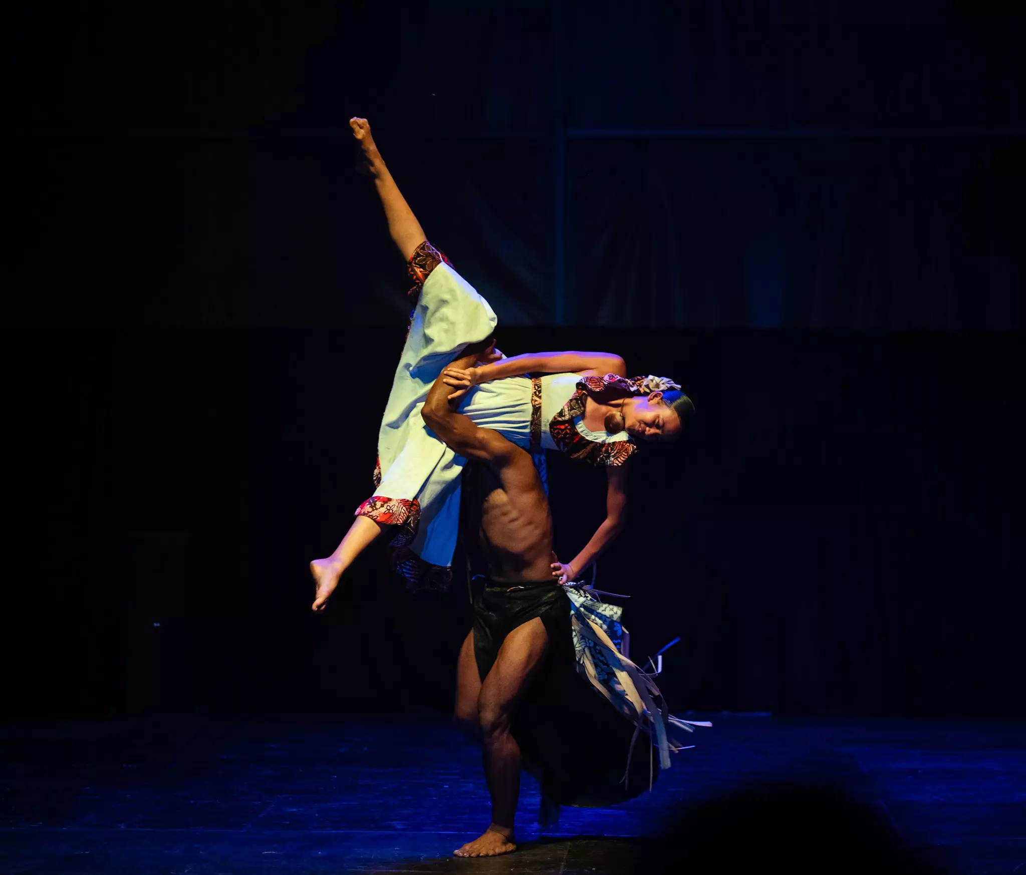 Two dancers perform on stage. One is lifted over the shoulder of the other.