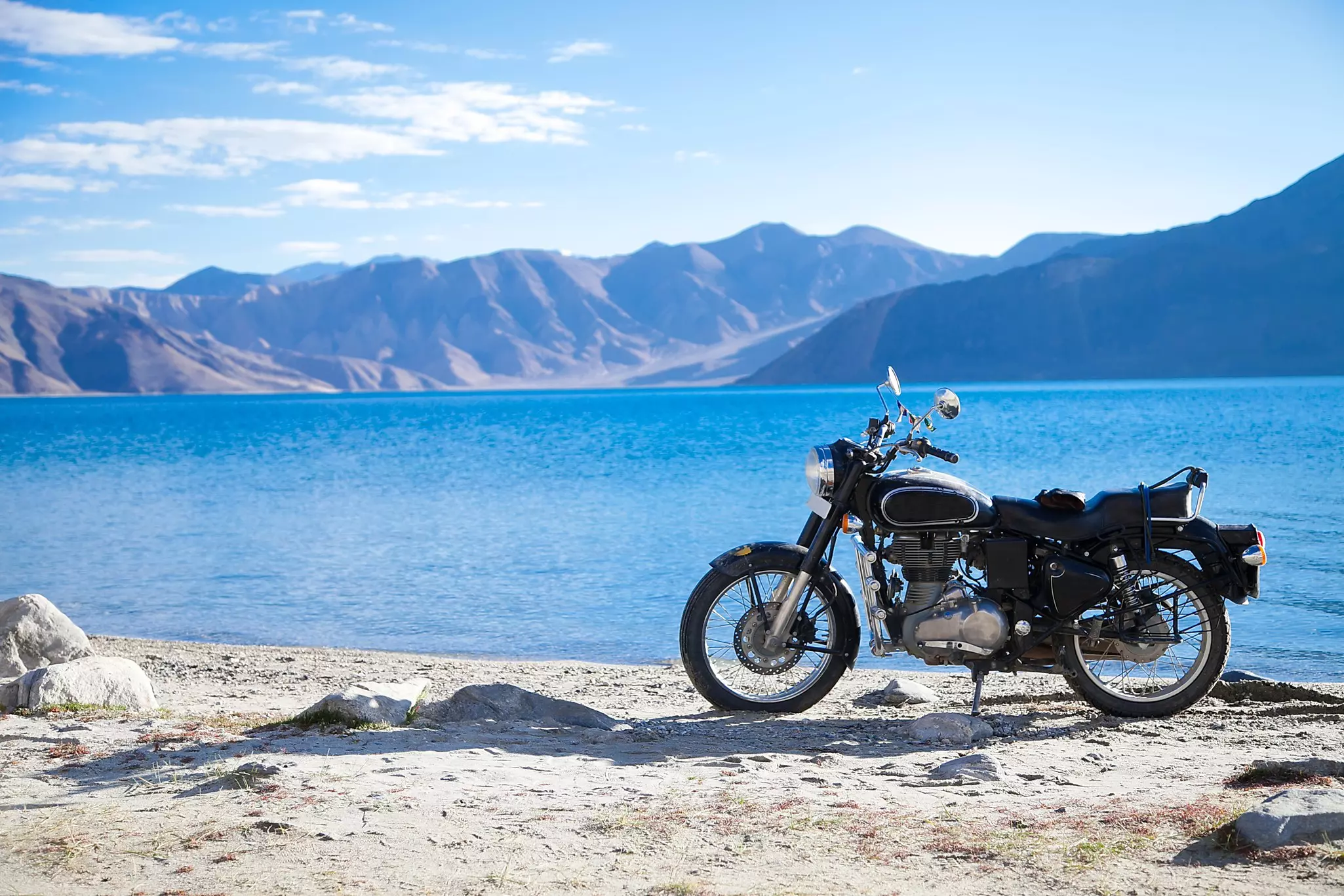 A motorbike parked beside a blue lake surrounded by mountains