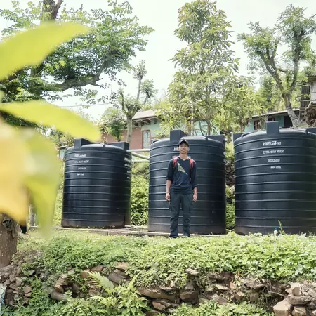 A Nepali man stands in front of rainwater harvesting tanks.