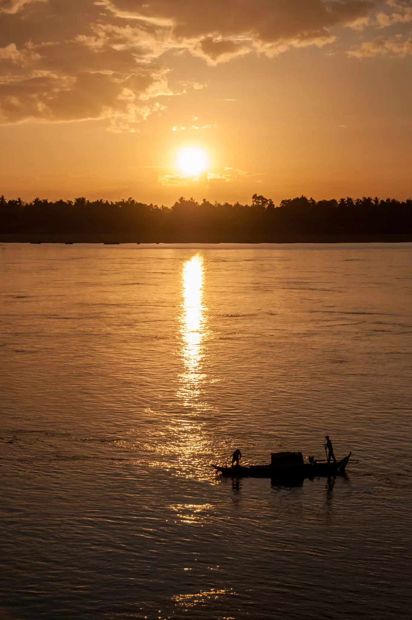 a boat sails at sunset on a river in Cambodia