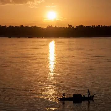 a boat sails at sunset on a river in Cambodia