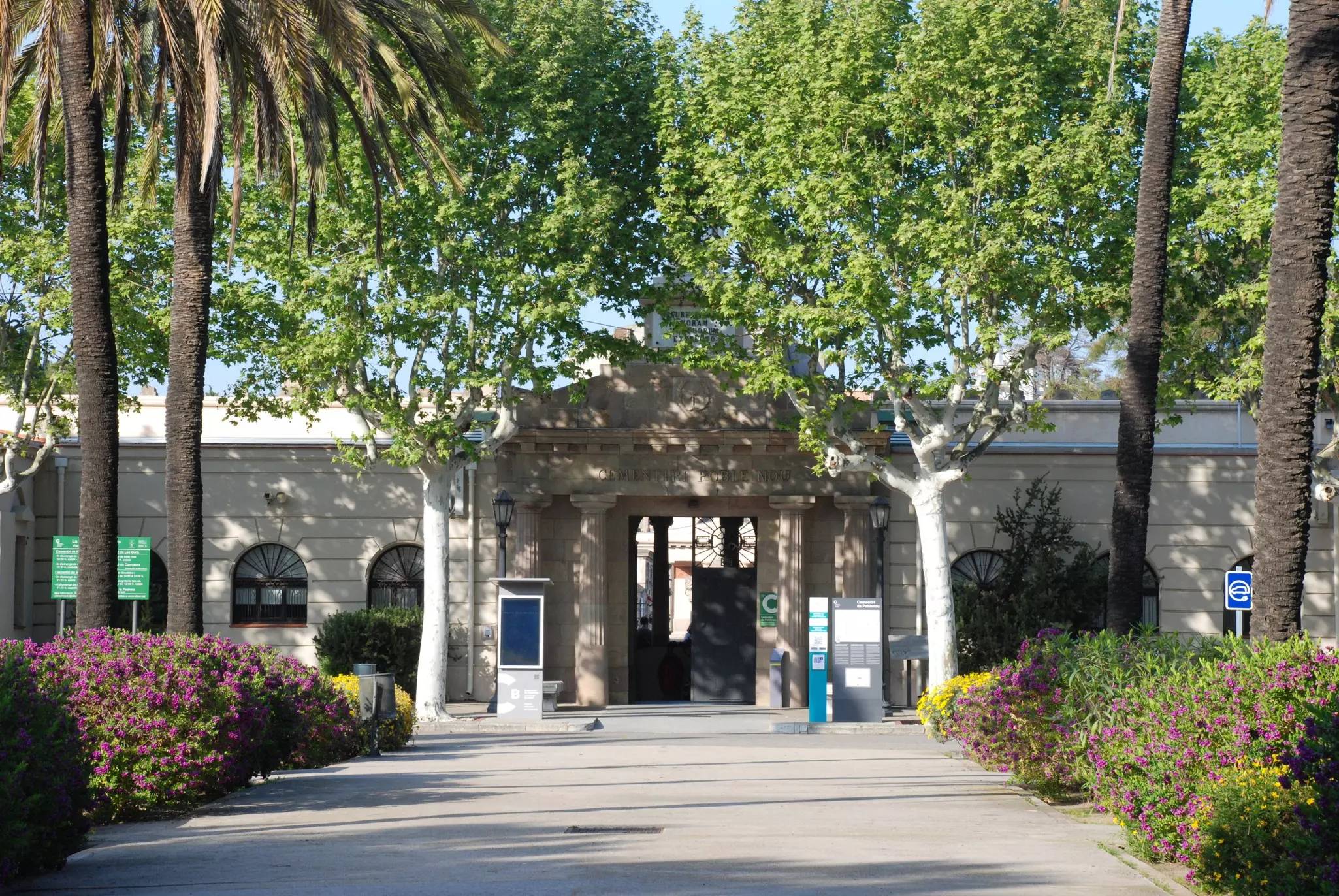 Entrance to Cemintiri del Poblenou with trees and floral bushes nearby.