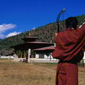 Archer in traditional dress drawing bow in archery competition at national archery ground, Changlimithang Stadium.
