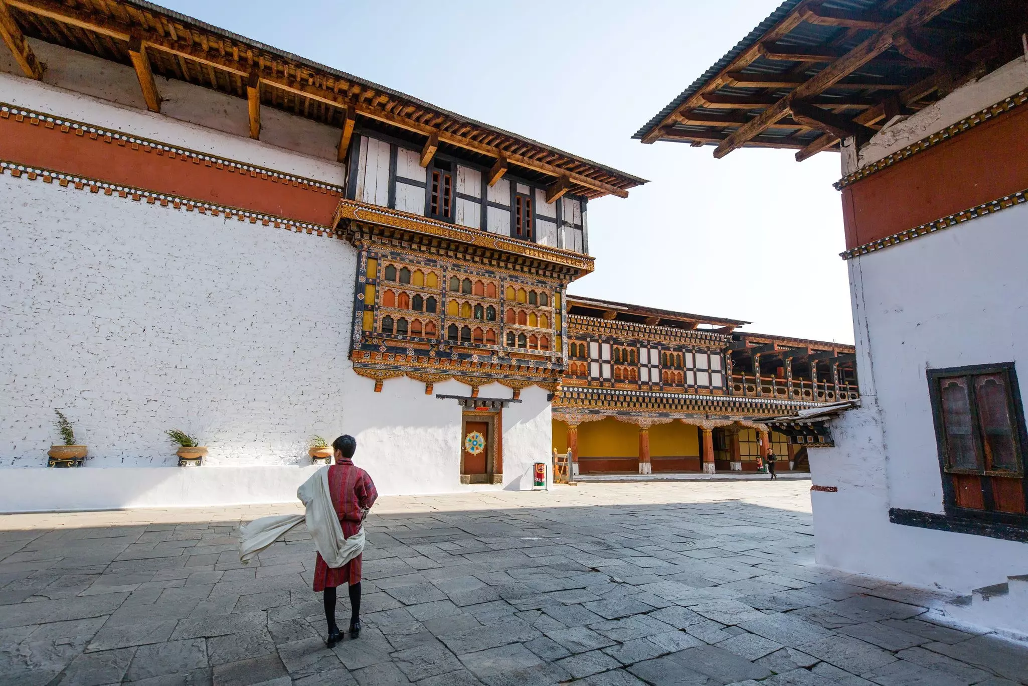 A guide in traditional Bhutanese dress walks through a monastery courtyard