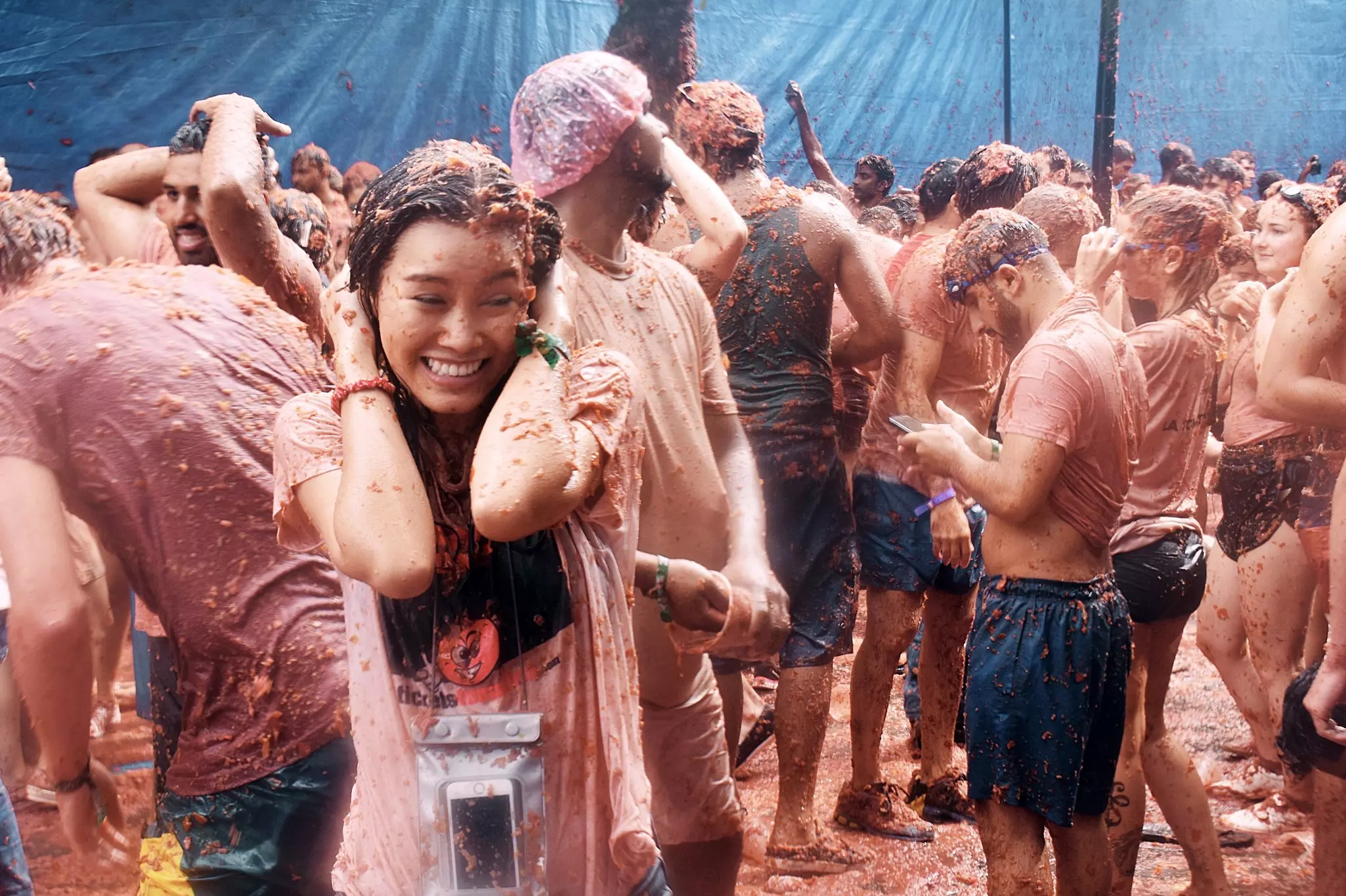 A woman smiling among a crowd of people throwing tomato pulp at a festival in Spain