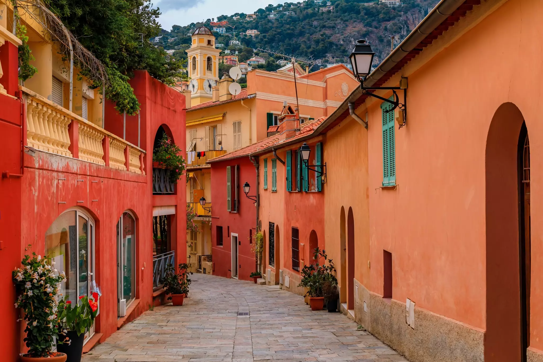 A cobblestone street in a town. All the buildings are painted in reds, oranges and ochers