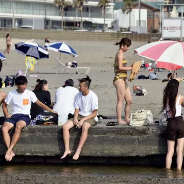 People sit on a wall at a beach near a city.