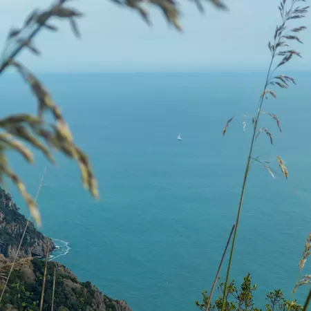 A view of crystal blue waters with one tiny sailboat. Photo taken from high on a cliff