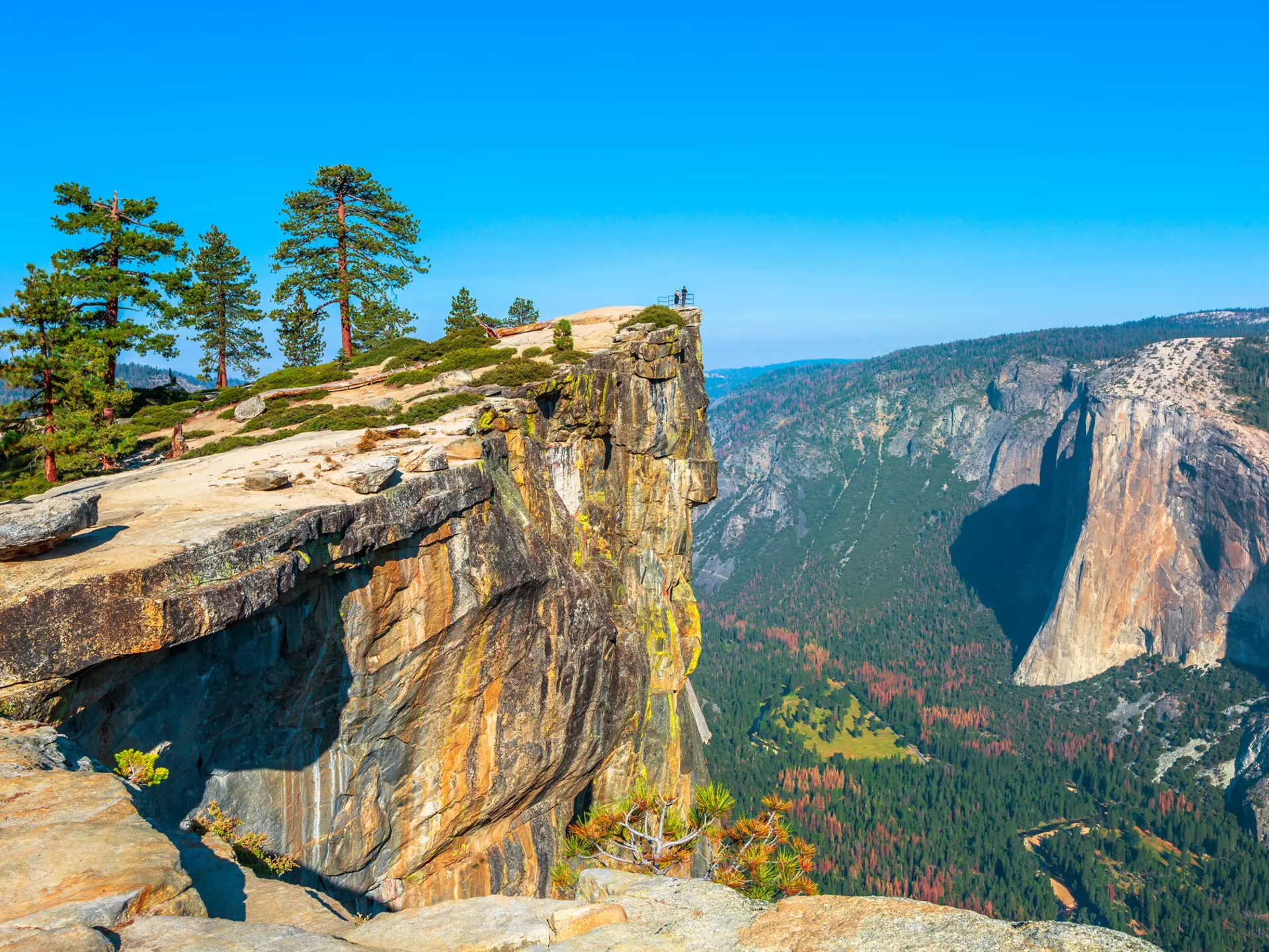 Panaramic view of verdant mountains. Two figures are barely discernable at the edge of a colorful point.