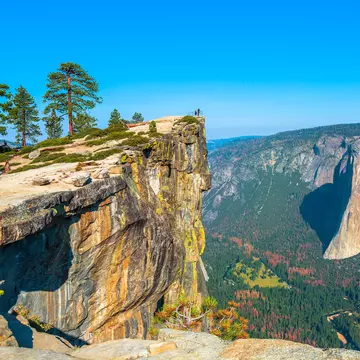 Panaramic view of verdant mountains. Two figures are barely discernable at the edge of a colorful point.