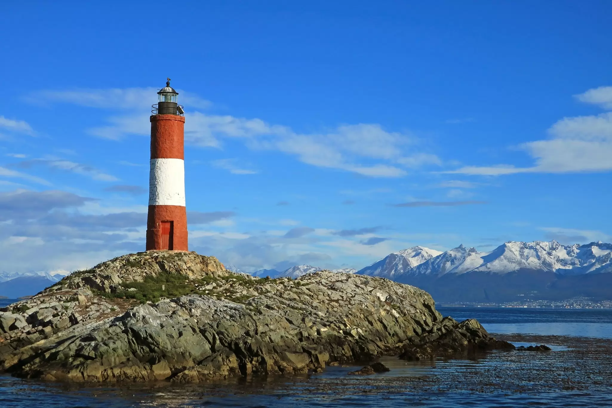 Ngọn hải đăng Les Éclaireurs gần Ushuaia, Argentina, với những dãy núi phủ tuyết trắng phía sau, trên mặt nước.