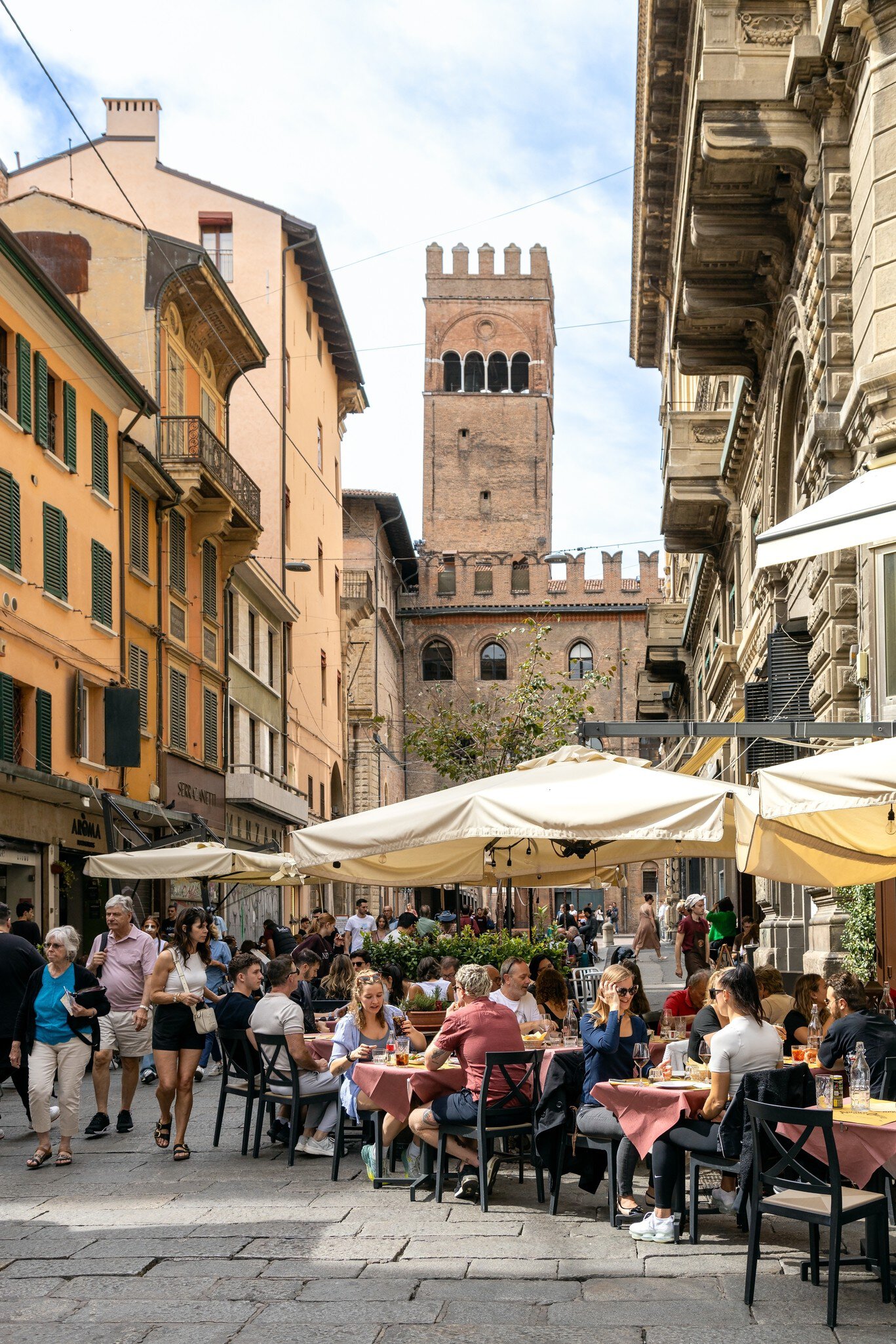 Bologna, Italy - Sep 15th, 2024: Busy street with people enjoying outdoor dining and the Torre dell'Arengo in the background