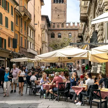 Bologna, Italy - Sep 15th, 2024: Busy street with people enjoying outdoor dining and the Torre dell'Arengo in the background