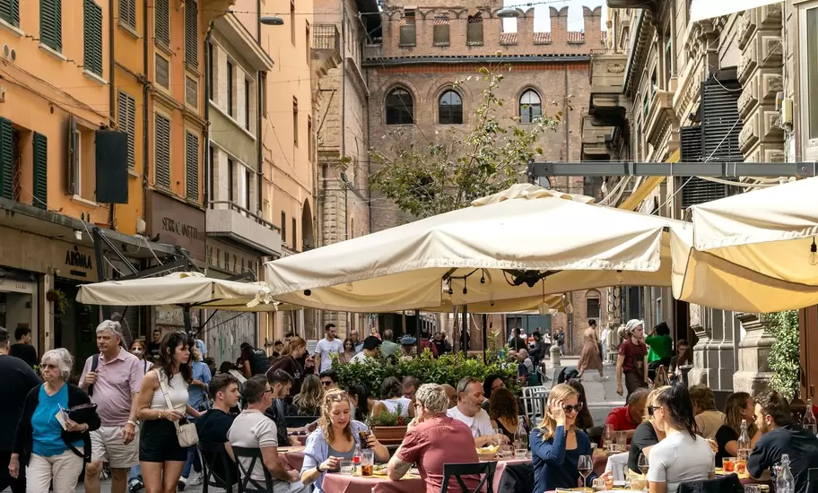 Bologna, Italy - Sep 15th, 2024: Busy street with people enjoying outdoor dining and the Torre dell'Arengo in the background