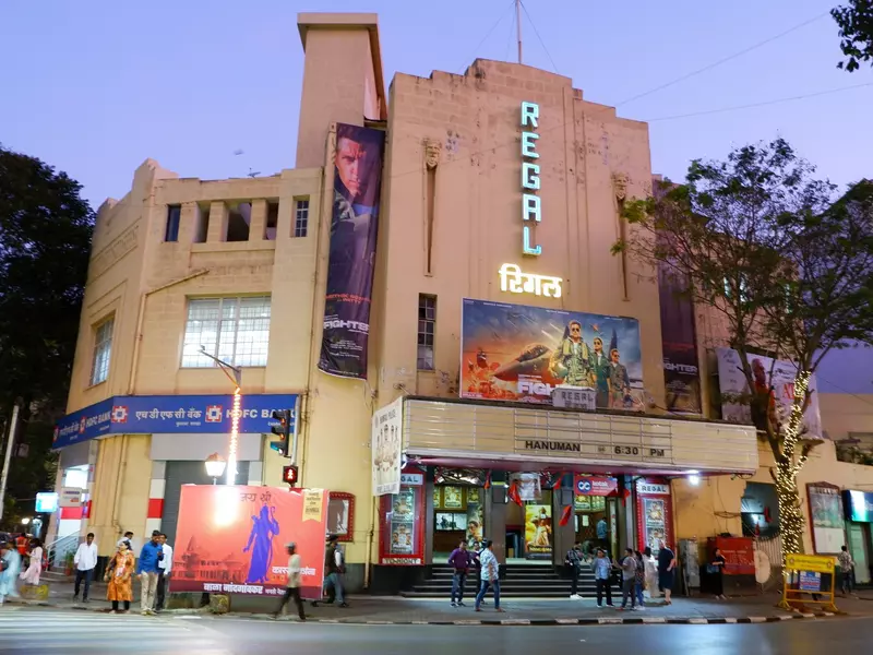 A movie theater in India at night has a vertical sign reading "Regal" lit up and a marquee.