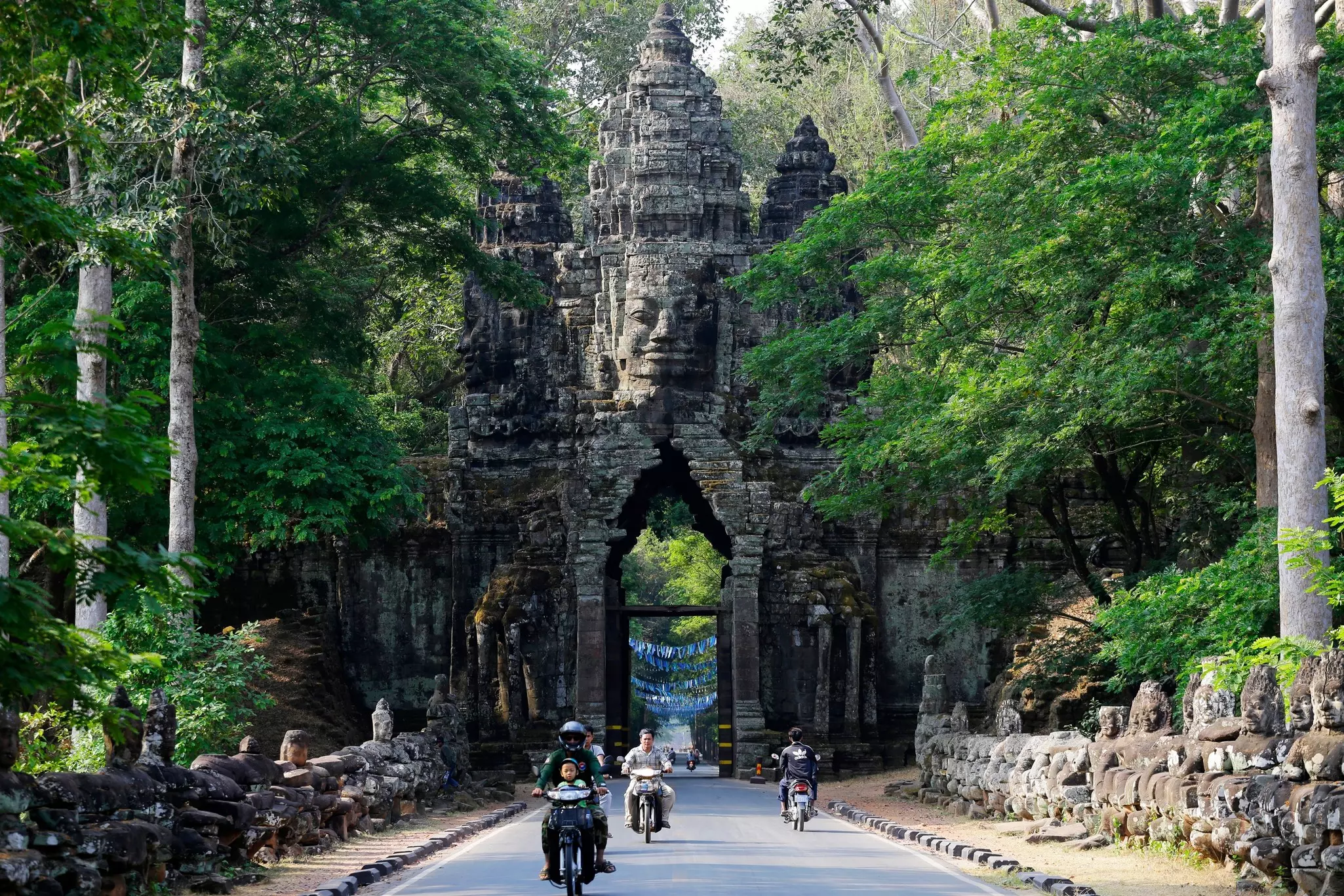 People ride motorcycles at a carved stone temple gate in Cambodia.