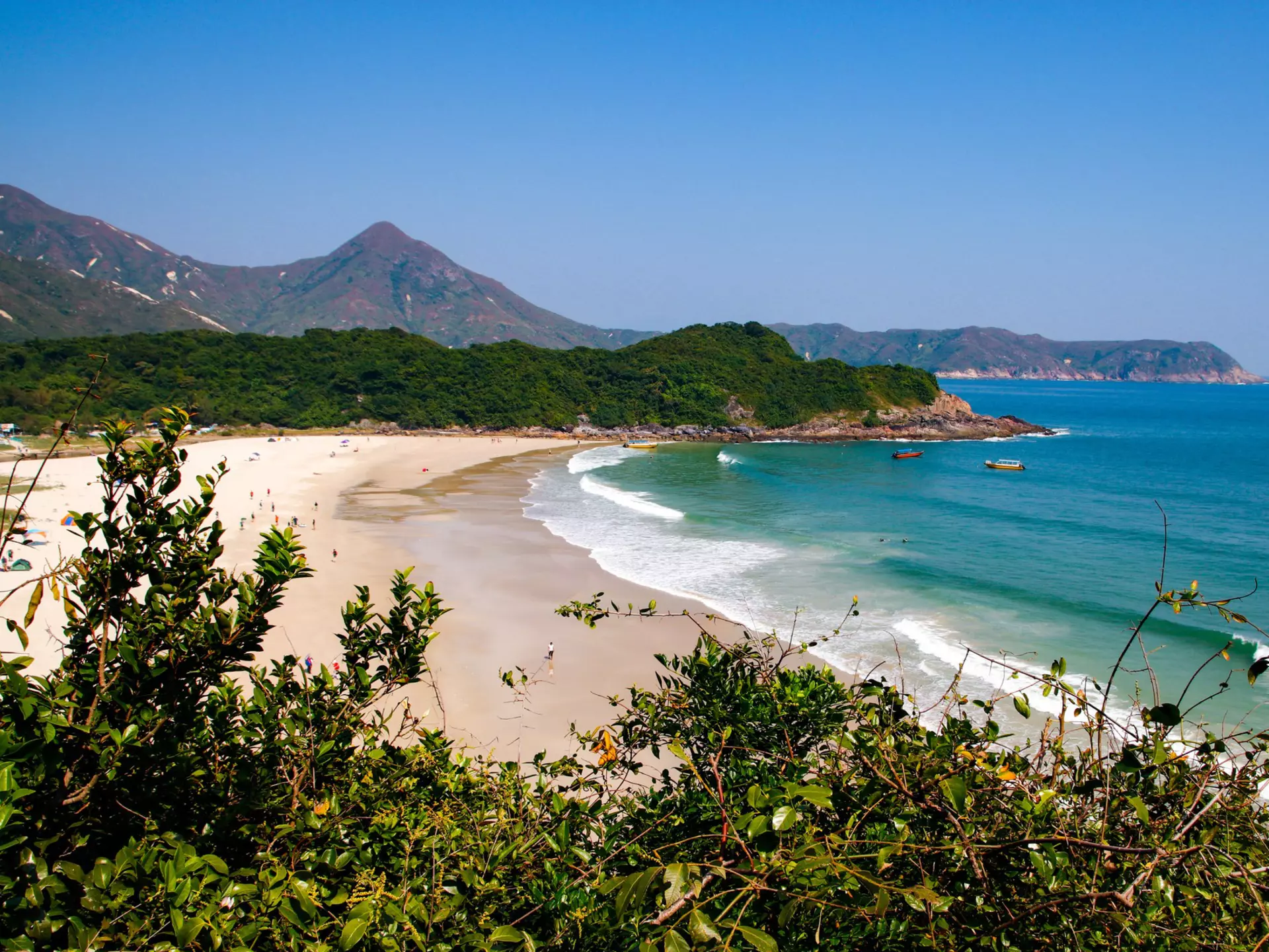 A wide sandy beach surrounded by mountain peaks.